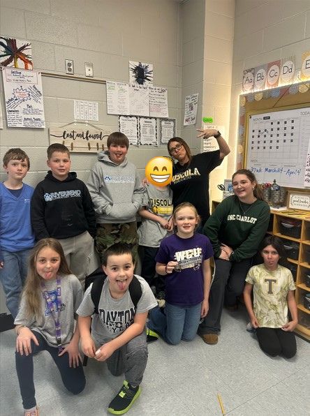  A group of students sticking out their tongues and wearing t-shirts from various high schools and colleges.  