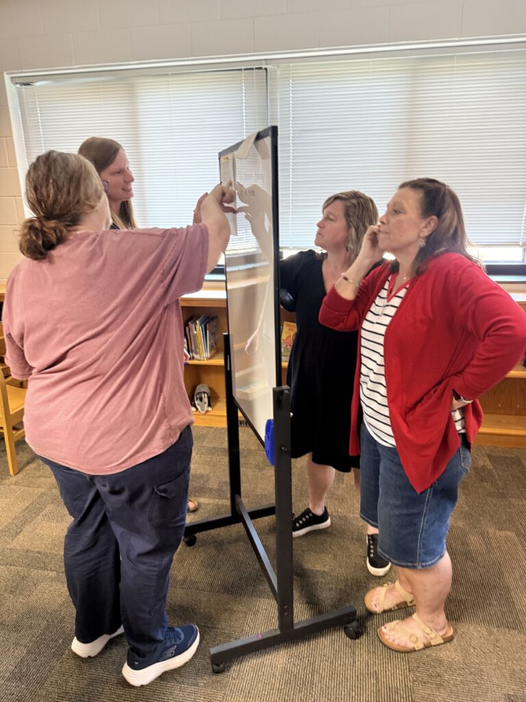 Four  teachers standing around a small white board working on a Math problem. 