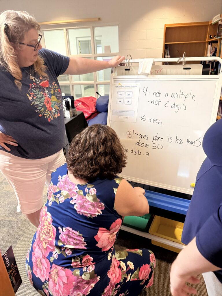 Three teachers standing around a small white board working on a Math problem. 