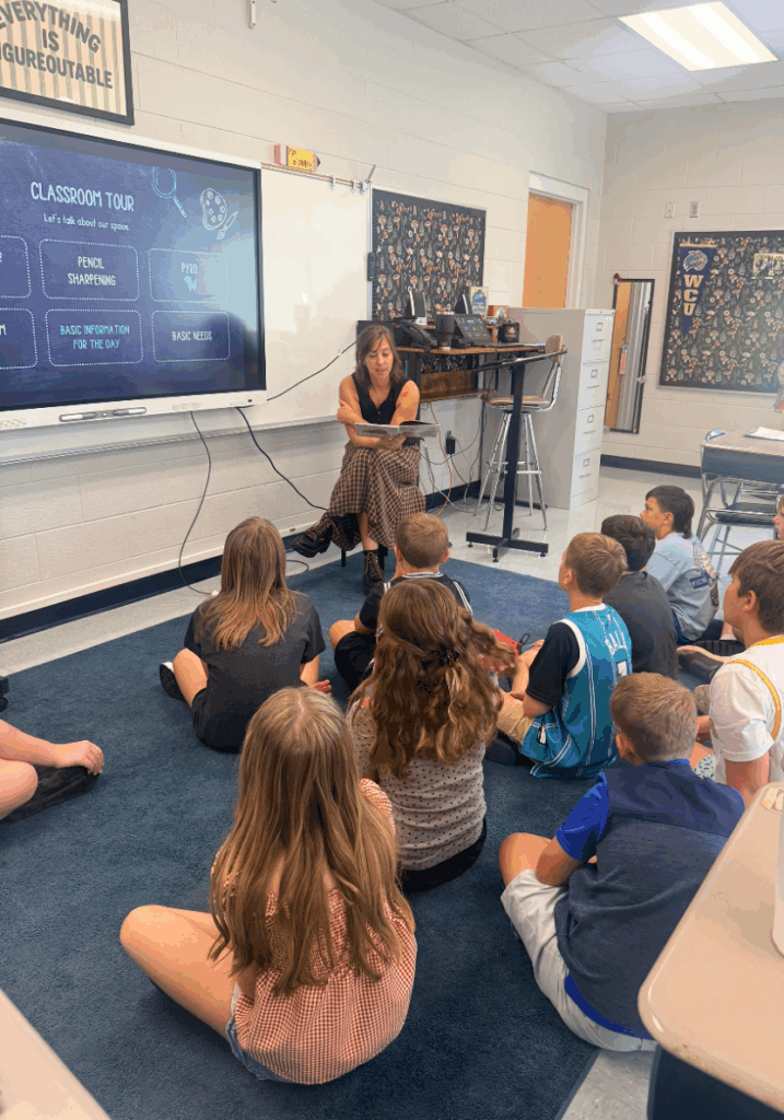 A teacher sharing first day read aloud with her students while they sit on the carpet at the front of the classroom. 